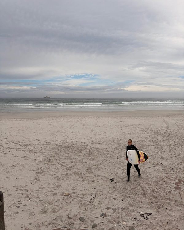 Sofia walking up the beach with a surfboard
